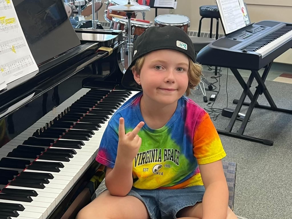 teen boy in grey hoodie sitting at grand piano